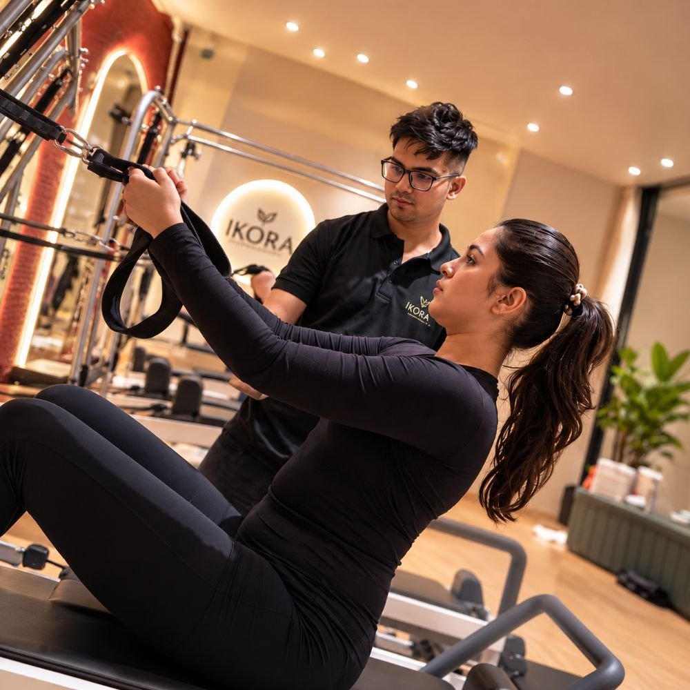 Instructor guiding a member on the reformer beneath the IKORA sign